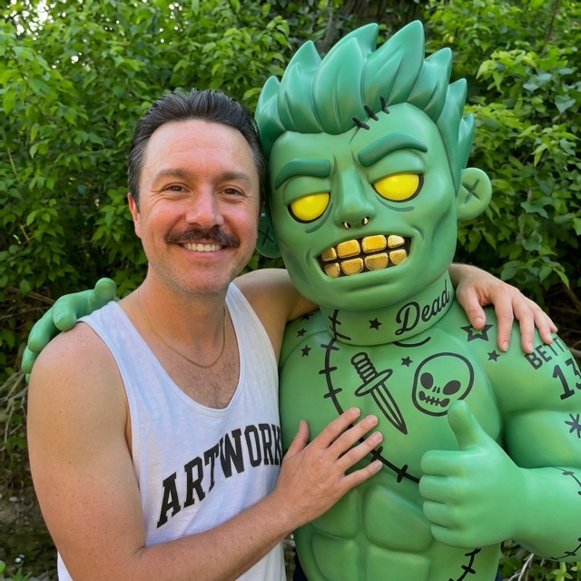 Drew, grinning, arm around a large green zombie mascot.